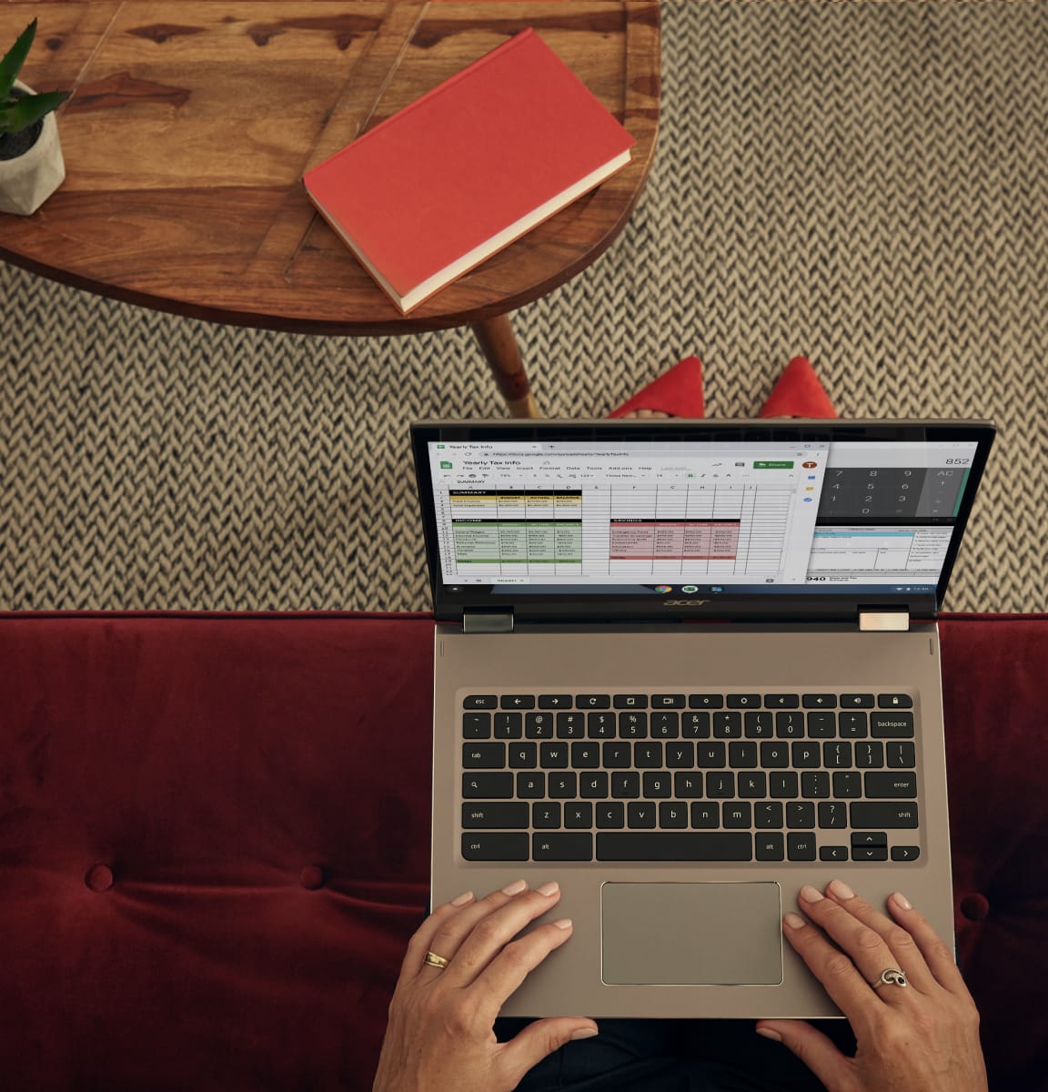 Hotellissa punaisella sohvalla istuva punakenkäinen nainen tekee töitä Chromebookilla.
